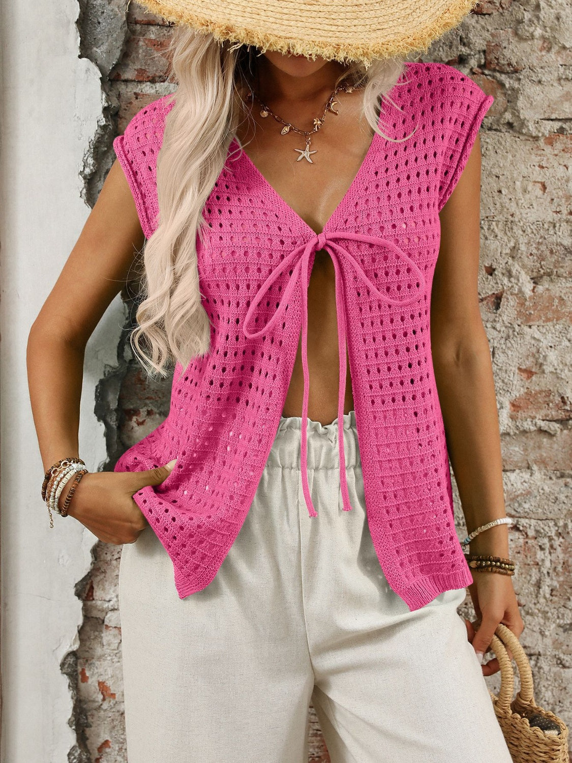 Fuchsia pink open-knit sleeveless cardigan with tie-front detail and deep V-neckline.