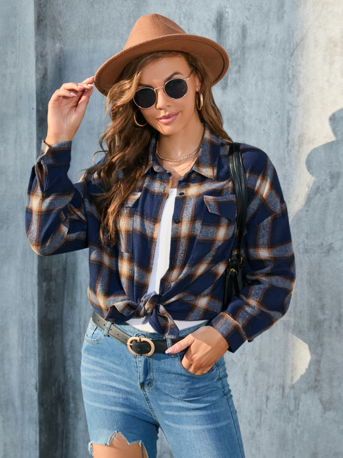 Plaid button-up shirt in dark blue with tan and white plaid, featuring chest pockets and a knotted hem.