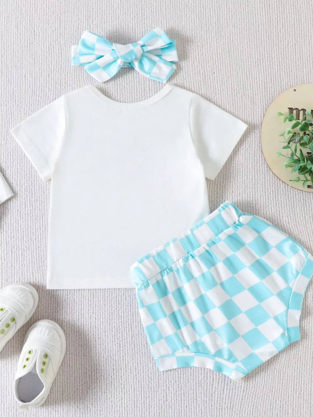 Baby girl outfit: white t-shirt and blue checkered shorts with matching bow headband.