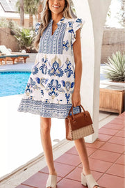 White mini dress with blue floral print, ruffled sleeves, and tiered hem.