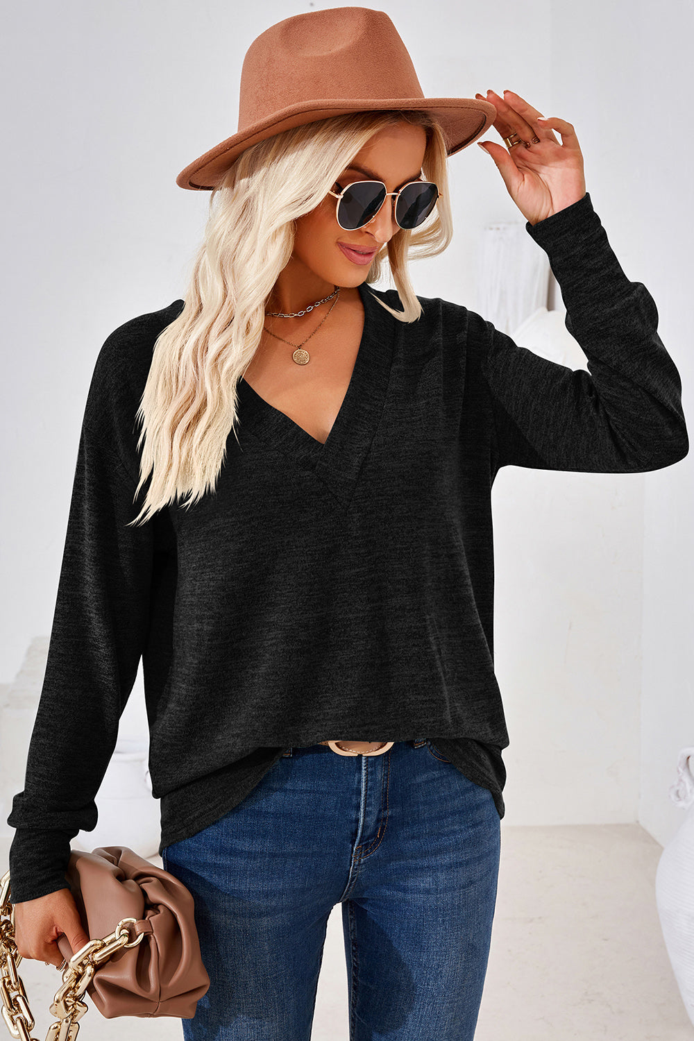 Black relaxed V-neck tunic top with long sleeves, styled with jeans and a hat.