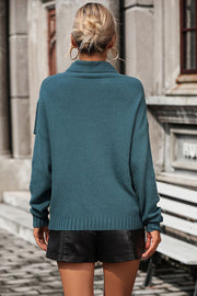 Deep teal knit turtleneck sweater with fringe detail on shoulders and ribbed trim.