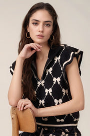 Black knit zip vest with allover bow pattern and contrast trim