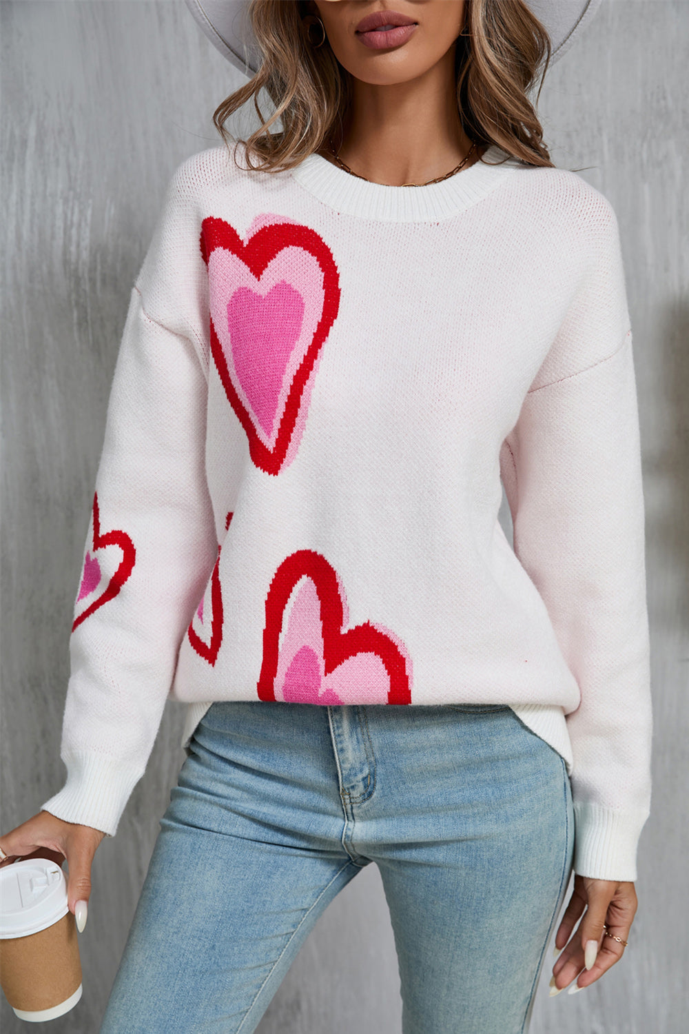 White intarsia knit sweater with multi-color heart motif, crew neck, and long sleeves.