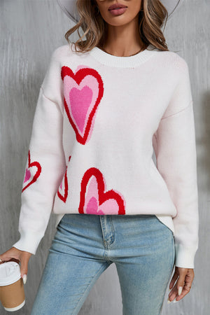 White intarsia knit sweater with multi-color heart motif, crew neck, and long sleeves.