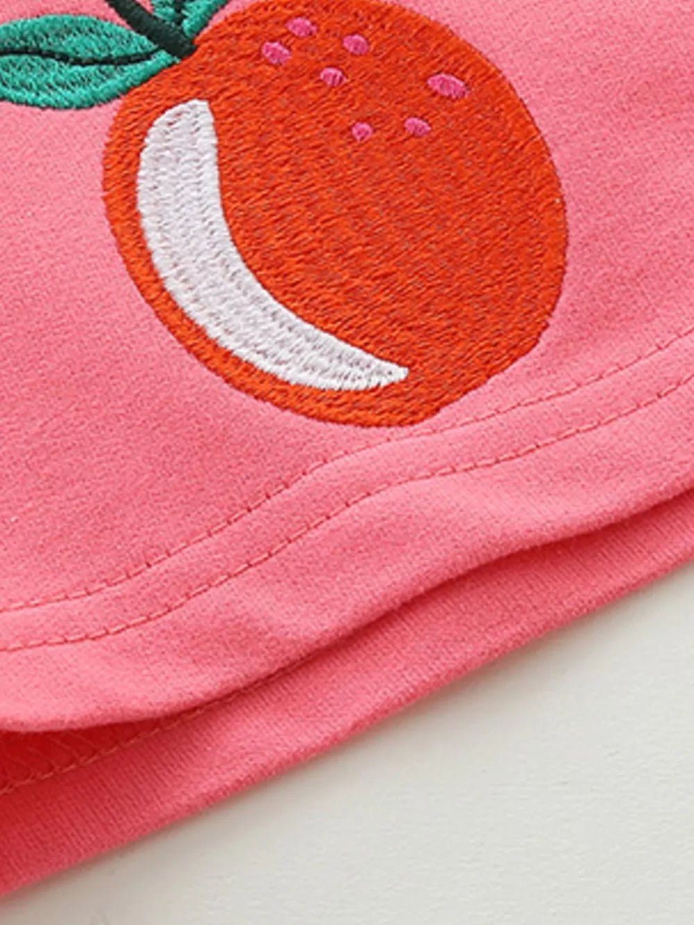 Pink cotton baby shorts with embroidered orange fruit detail.