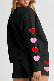Black quilted loungewear set with red and pink heart appliqués on the sleeves and shorts.