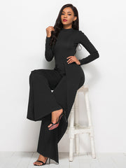 Black high-waisted palazzo jumpsuit with slit front and long sleeves.