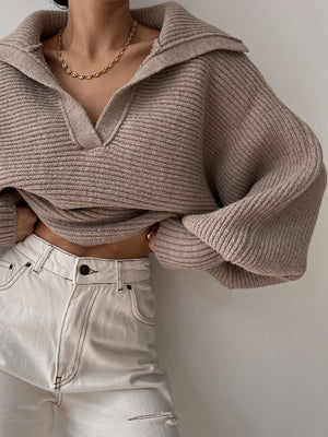 Tan knit sweater with wide collar and balloon sleeves, featuring a V-neck and ribbed texture.