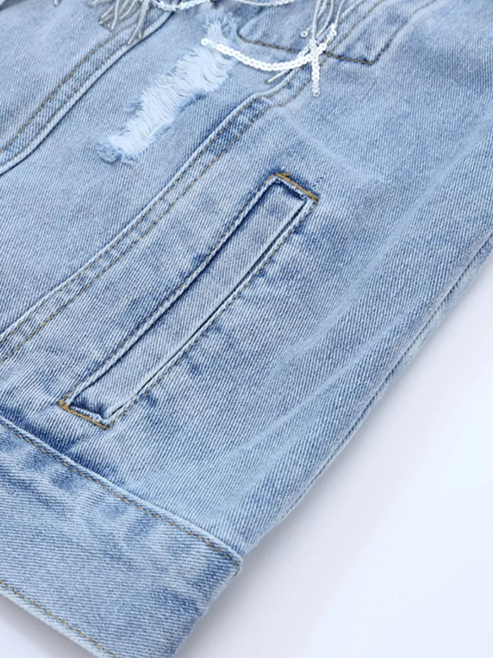 Light wash denim trucker jacket with distressed details, sequin fringe, and pocket.
