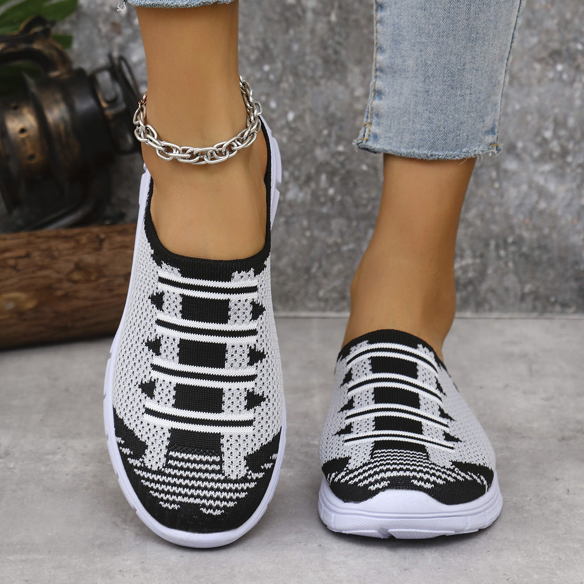 White and black knit slip-on sneakers with decorative lacing detail.