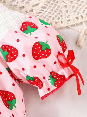Baby pink one-piece with strawberry print, smocked detail, and red ribbon bows on sleeves.