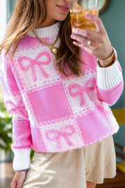 Fuchsia pink checkered bow jacquard knit sweater with white cuffs and neckline.