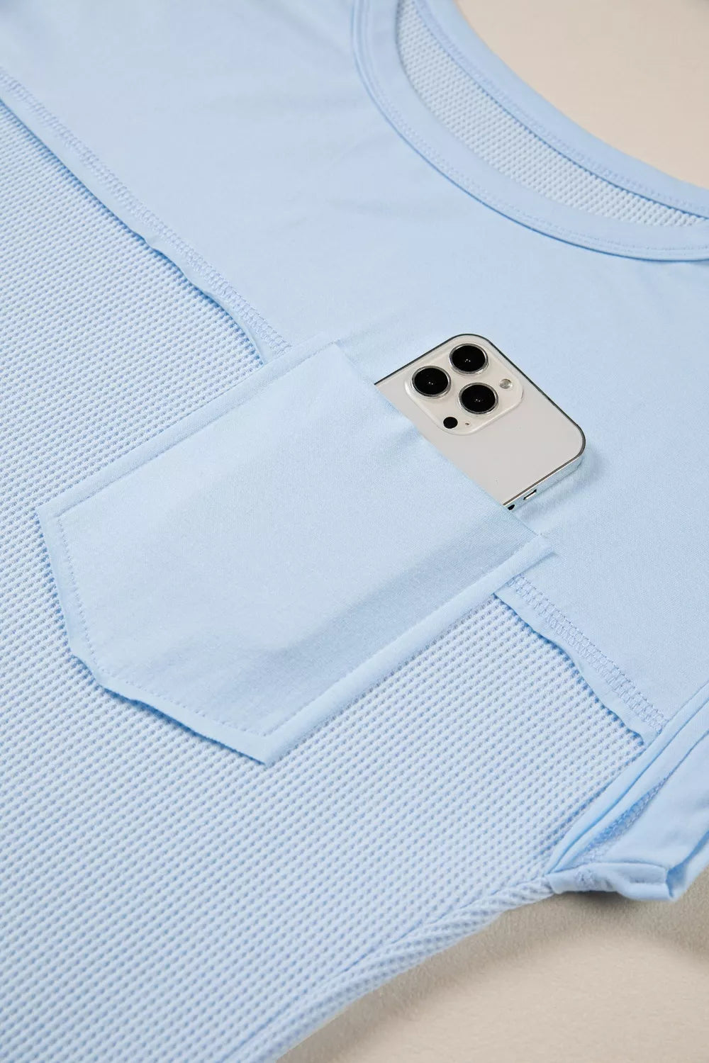 Light blue waffle knit t-shirt with pocket holding a phone and curved hem detail.