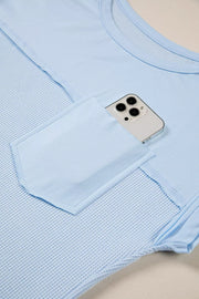 Light blue waffle knit t-shirt with pocket holding a phone and curved hem detail.