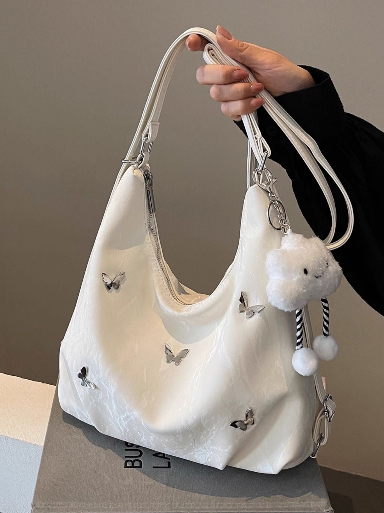 White shoulder bag with butterfly appliques and a cloud charm with pom poms.