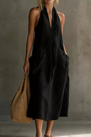 Black halter midi dress with V-neck and large front pockets, styled with a straw bag.