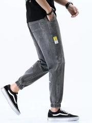 Men's grey relaxed fit drawstring jeans with cuffed ankles and a yellow tag detail.