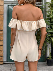 Tan ruffled off-shoulder romper with white pom-pom trim and bow-tie detail.