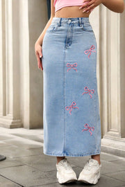 Light wash denim maxi skirt with pink bow embroidery and button closure.
