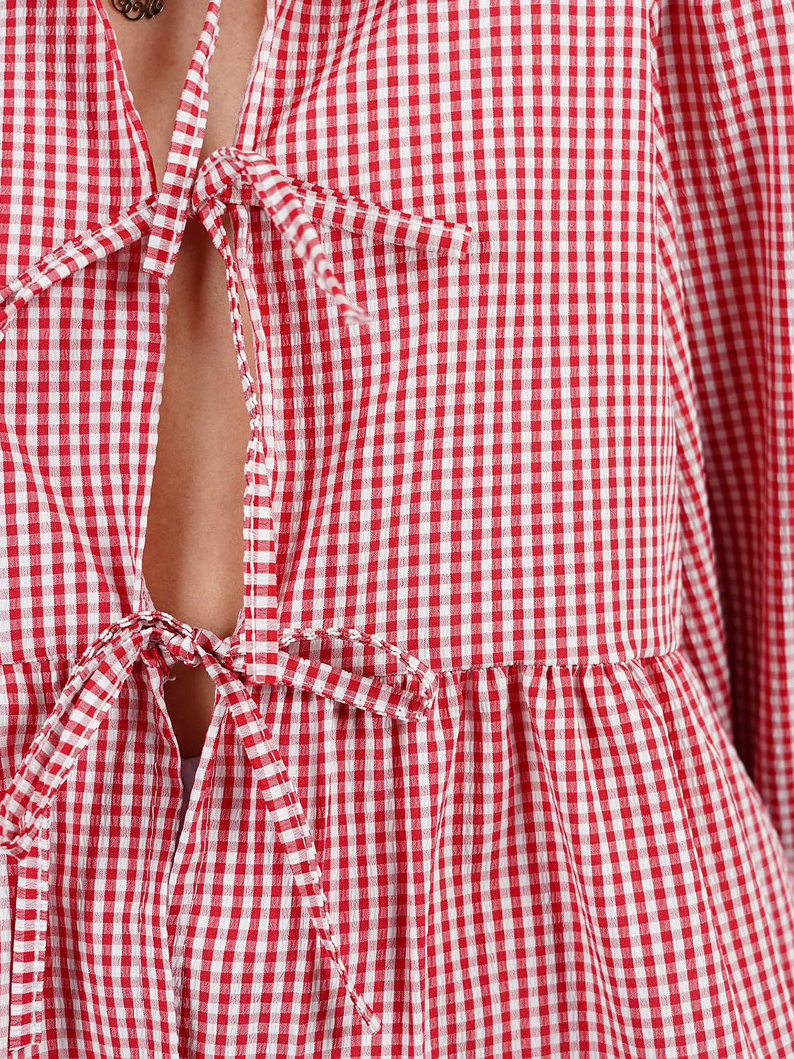 Red gingham tie-front peplum blouse with voluminous sleeves and a tie closure.