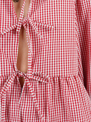 Red gingham tie-front peplum blouse with voluminous sleeves and a tie closure.