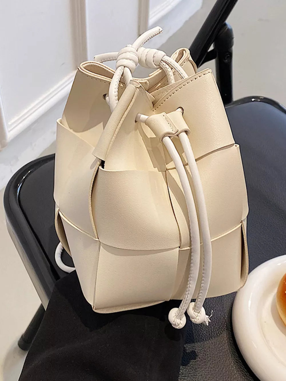 Chic woven mini bucket bag in white with drawstring closure and knotted handles.