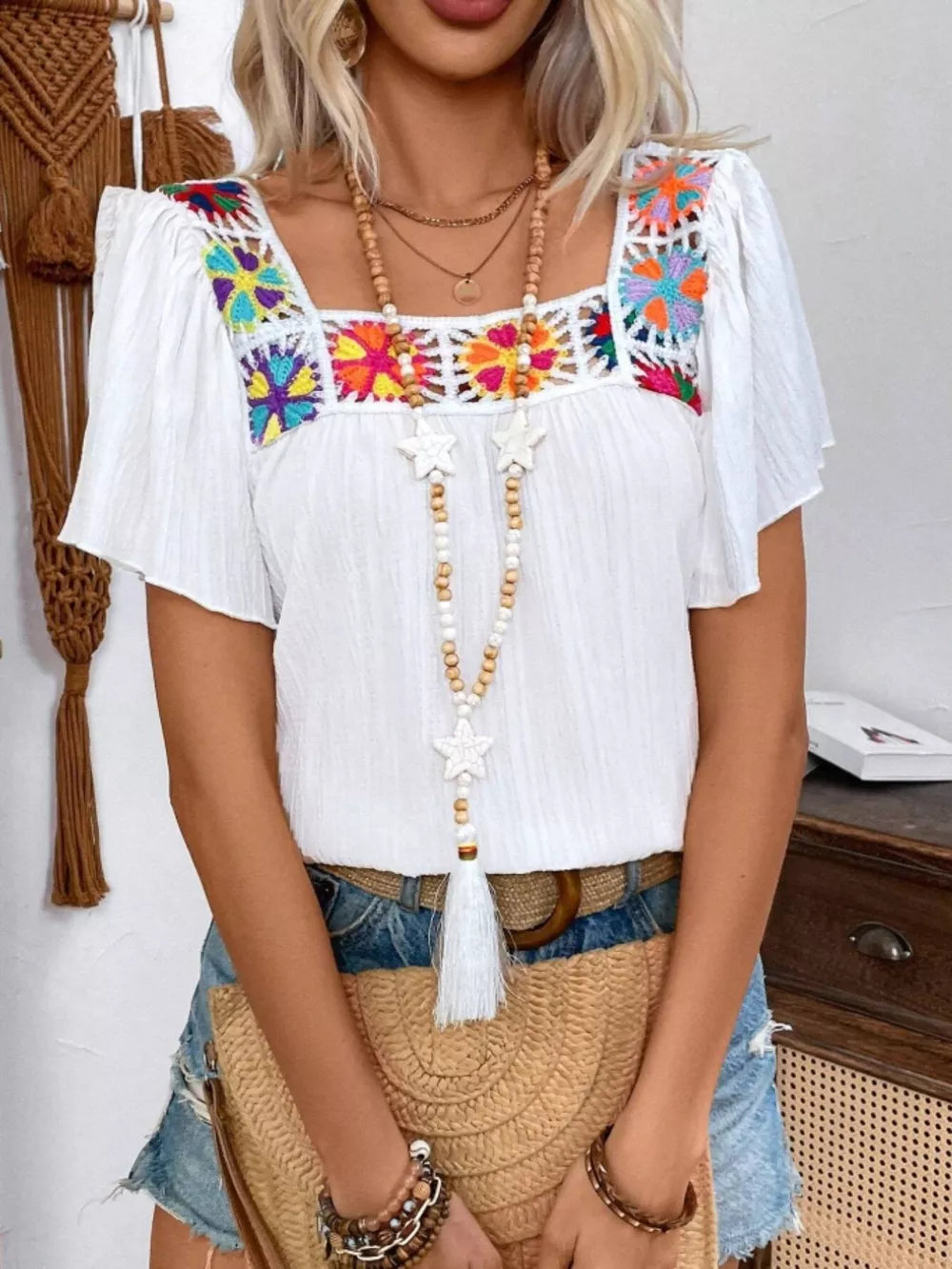 White embroidered square neck blouse with colorful floral crochet detail and flutter sleeves.