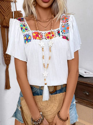 White embroidered square neck blouse with colorful floral crochet detail and flutter sleeves.