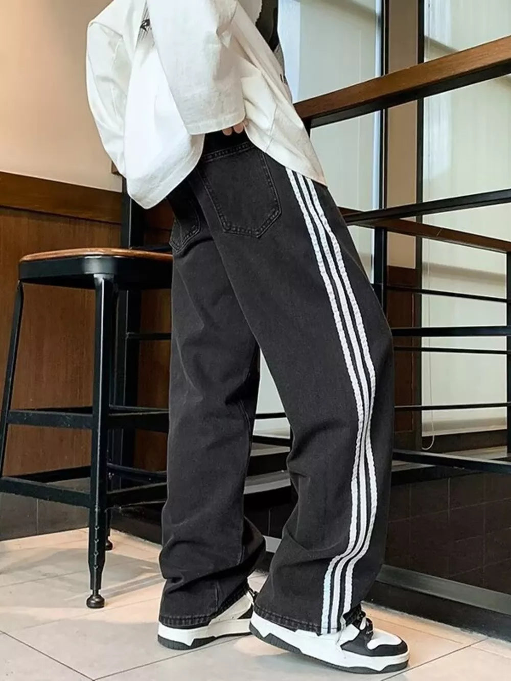 Men's black oversized wide-leg jeans with white side stripes.