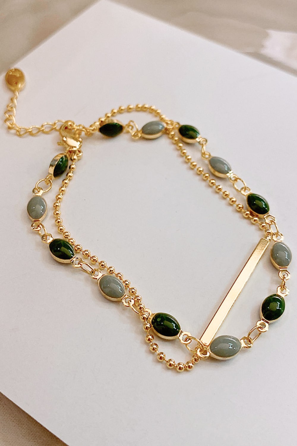 Gold dual chain bracelet with green and grey oval stones and a bar accent