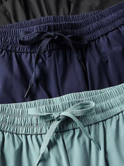 Men's drawstring active pants in black, navy, and turquoise with elastic waistbands.