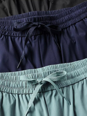 Men's drawstring active pants in black, navy, and turquoise with elastic waistbands.