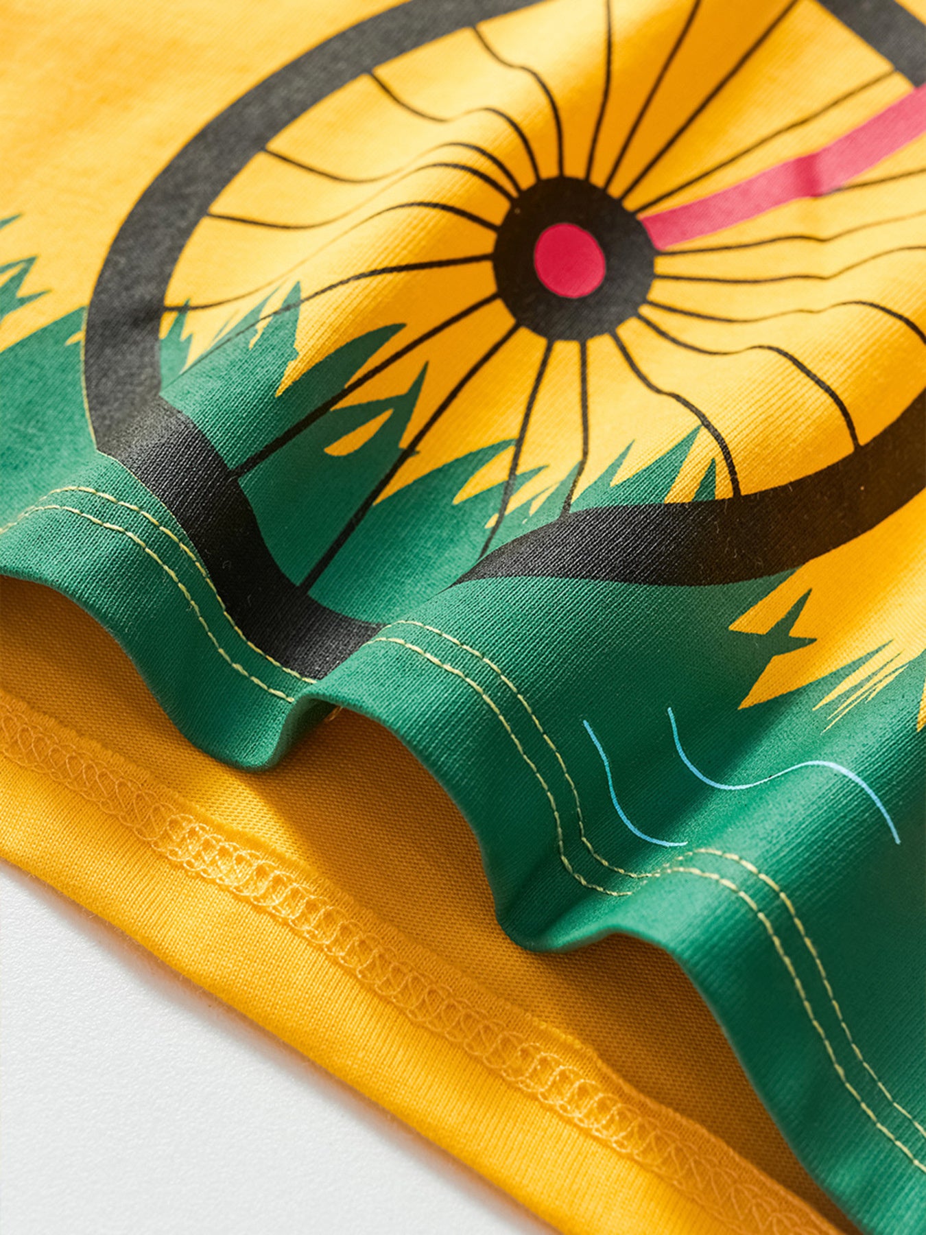 Yellow cotton t-shirt with bicycle wheel graphic and green grass detail.