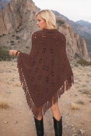 Brown knit poncho with geometric cutouts and fringe detail, acrylic material.