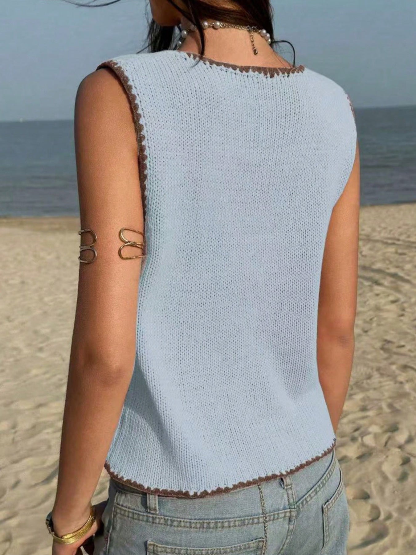 Light blue knit sweater vest with brown trim, sleeveless, crew neck, styled with jeans.