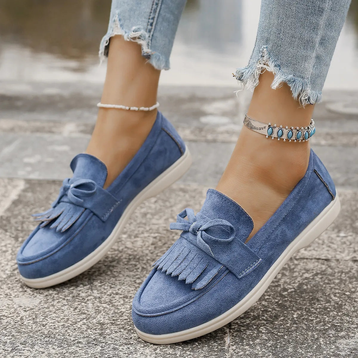 Dusty blue suede loafer flats with fringe and bow detail.