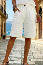 White pocketed knee-length shorts with elastic waist and button detail.