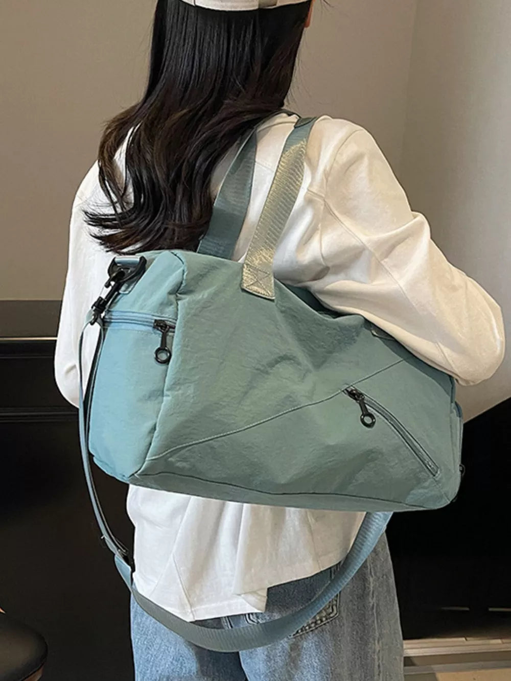 Teal duffel bag with multiple zippered pockets and adjustable straps, worn by a woman.