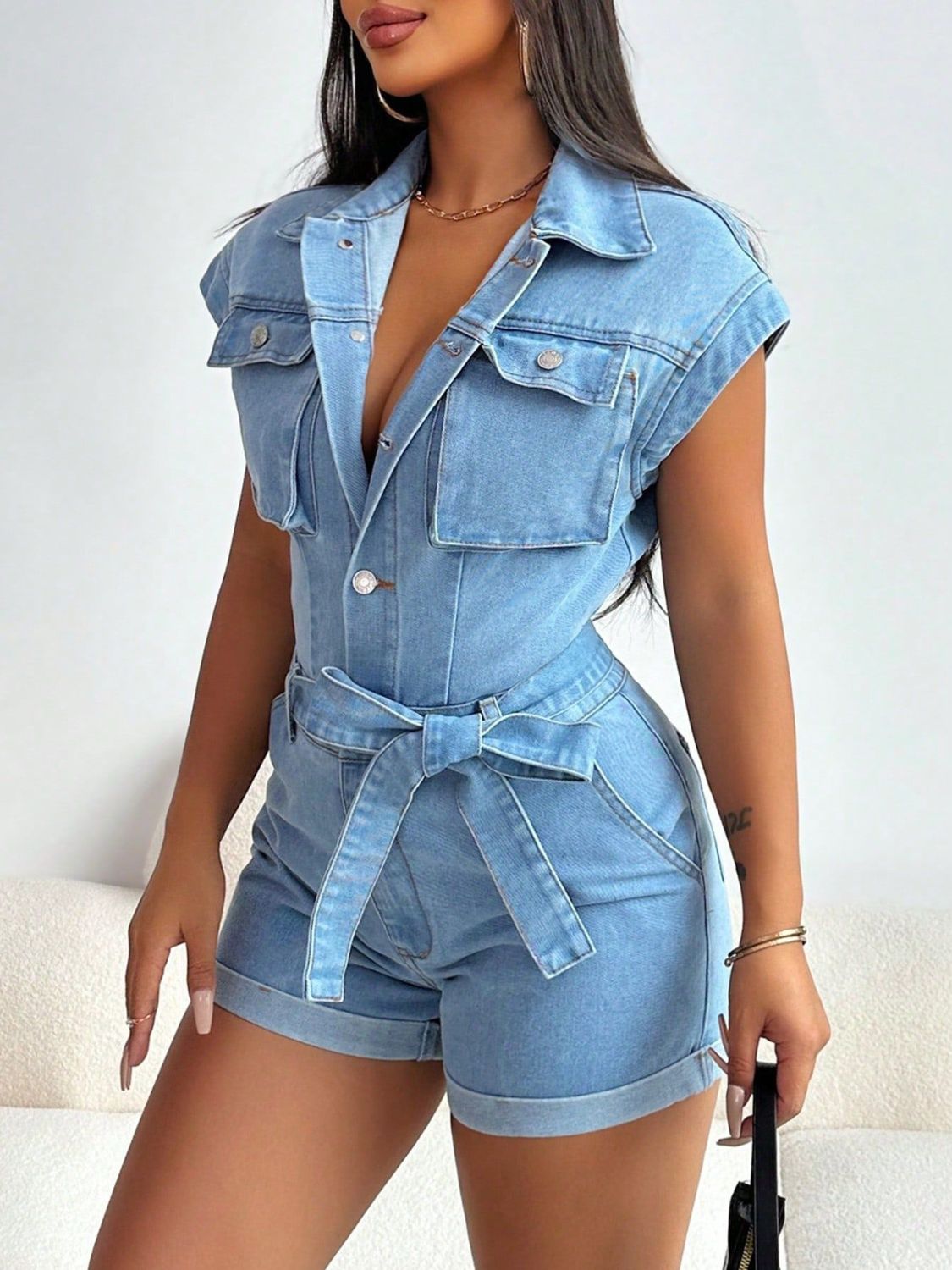Light wash denim romper with short sleeves, collar, chest pockets, and a tie waist.