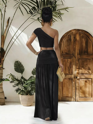 Black one-shoulder ruched crop top and maxi skirt set with cutout detail.