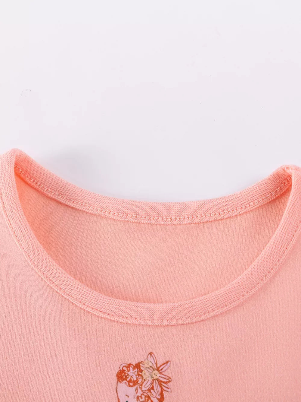 Peach cotton baby dress with fairy embroidery detail and rounded neckline.