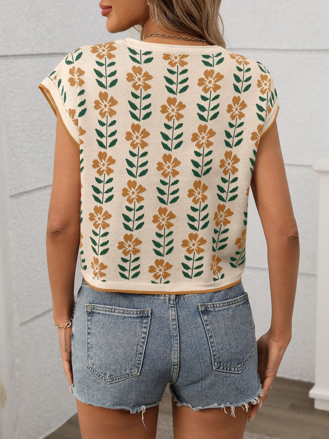 Floral knit sleeveless top in cream with orange flowers and green leaves pattern.