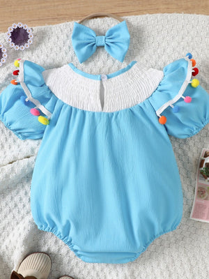 Pastel blue cotton baby romper with smocked white yoke, puff sleeves, and pom-pom trim. Includes matching bow headband.