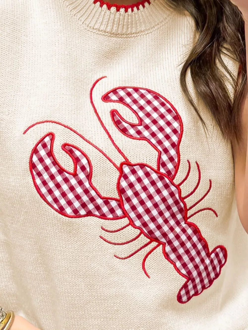 Beige knit sweater vest with red gingham lobster embroidery and red trim neckline.