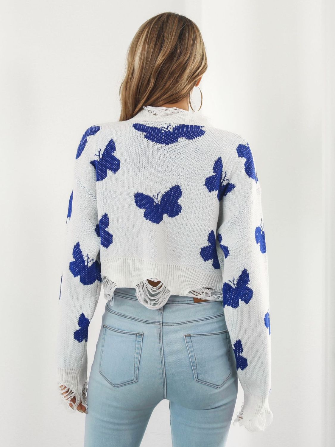 White cropped knit sweater with distressed details and a blue butterfly print.