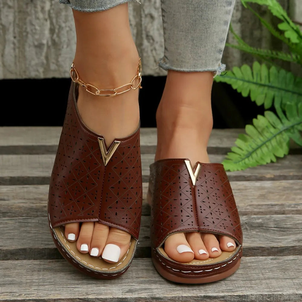 Brown laser-cut leather platform slides with V-shaped gold accent and open toe.