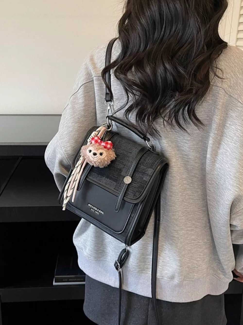 Chic black mini flap backpack with plush charm and adjustable strap.