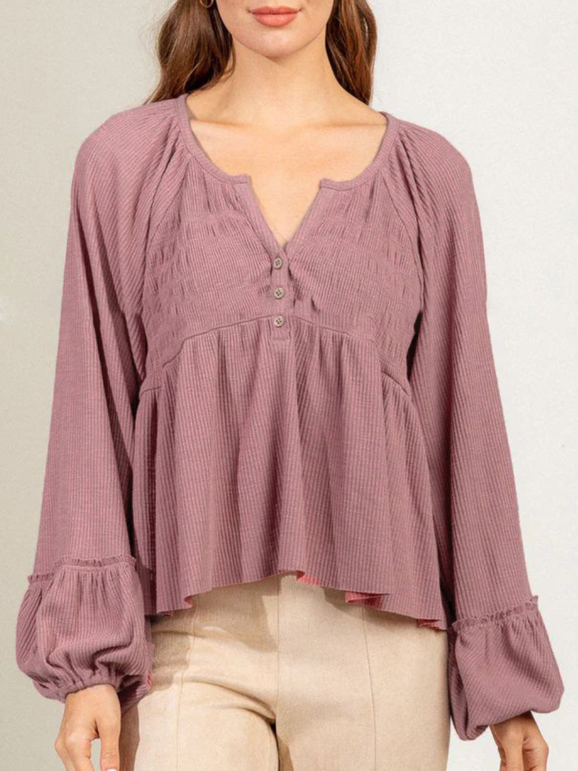 Textured ribbed peplum blouse in dusty pink with button detail, gathered neckline, and ruffled balloon cuffs.