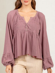 Textured ribbed peplum blouse in dusty pink with button detail, gathered neckline, and ruffled balloon cuffs.